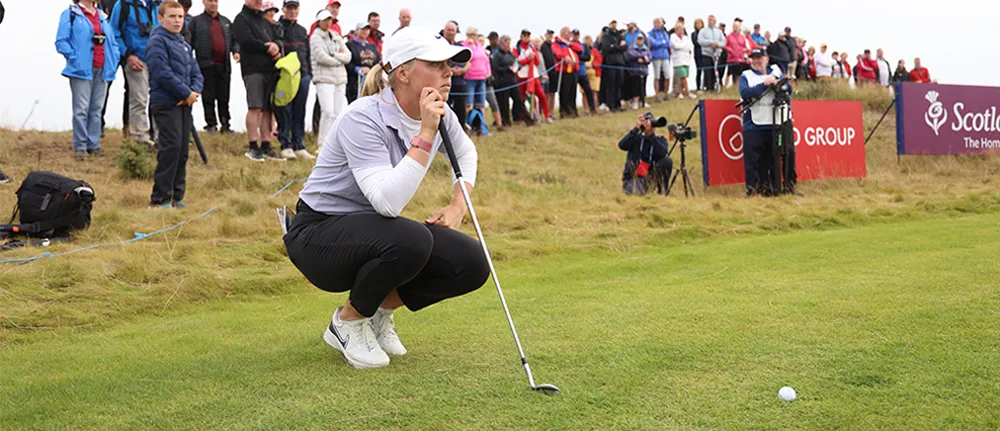 A crowd watches a woman golfer line up a shot.