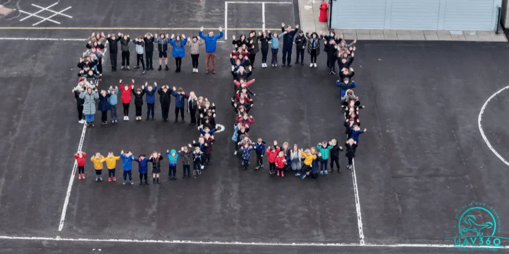 Pupils and staff pictured from above in a school playground creating the number 50 with their bodies
