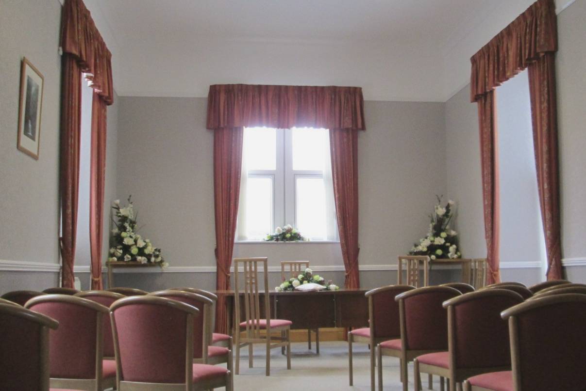 Old court room set up for wedding with cream flower displays and dusky pink chairs and draped curtains at the windows