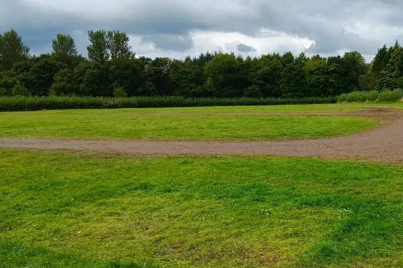 Grassy and hard standing event area surrounded by trees and shrubs