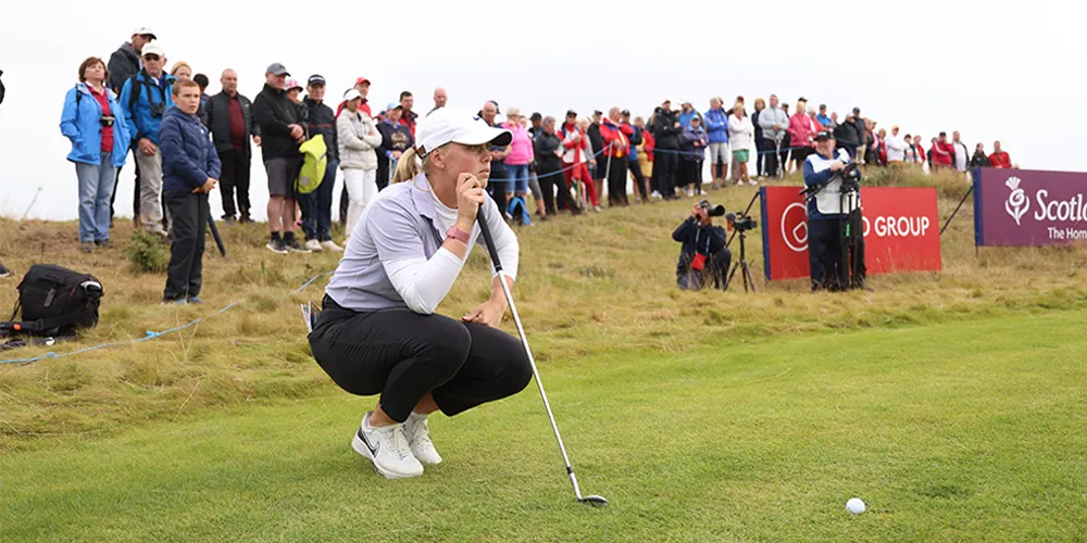 Golfer crouched on putting green with crowd in background