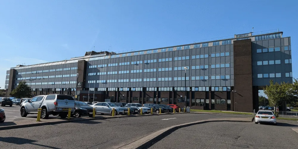 An image of the exterior of a large building on a sunny day with a number of cars in the foreground