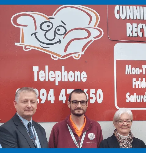 Two men and a woman stand in front of a red billboard.