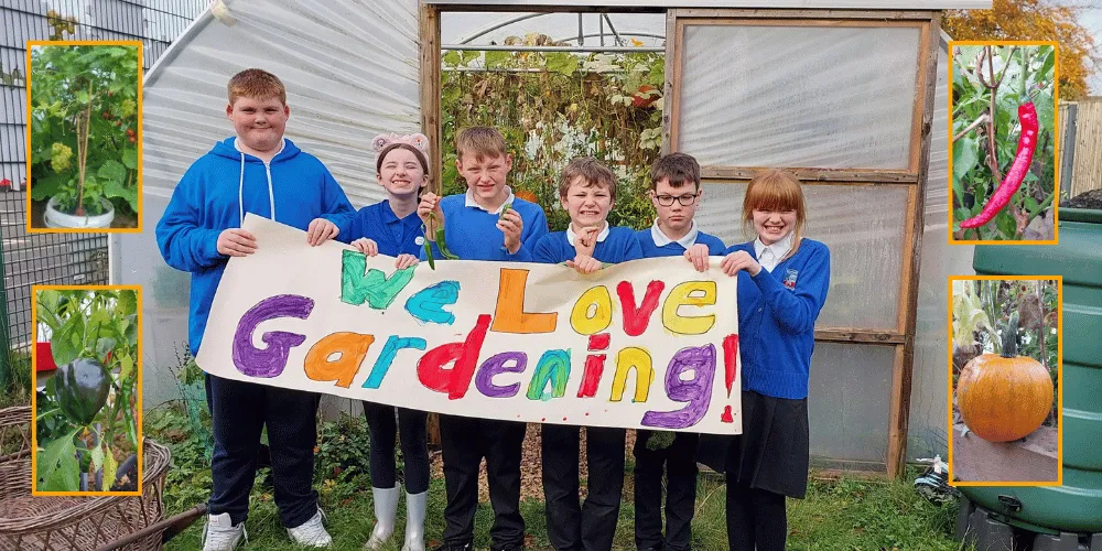 School children standing in front of a polytunnel holding a sign that says 'We Love Gardening'