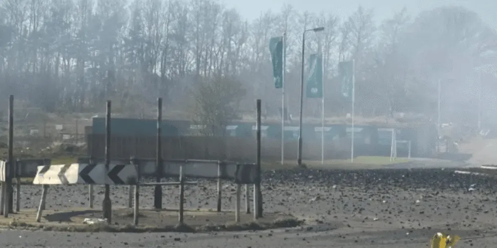 a roundabout and road showing the aftermath of a fire with a burned building in the background